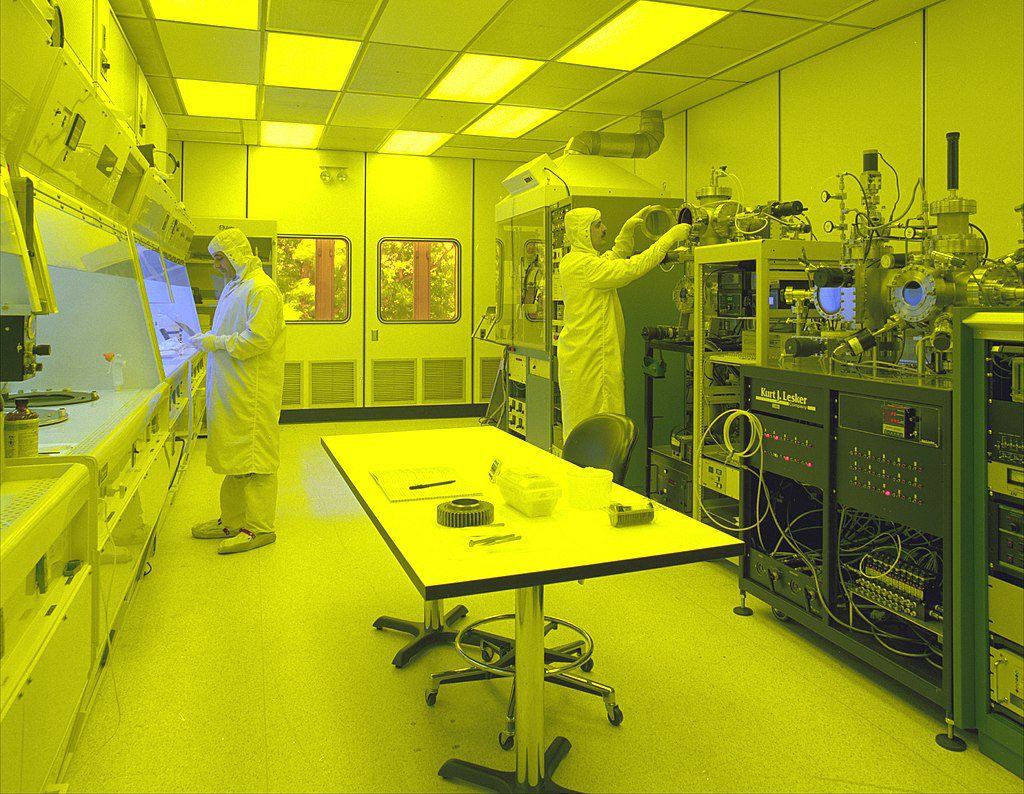 two researchers in a cleanroom under yellow light working with semiconductor manufacturing equipment